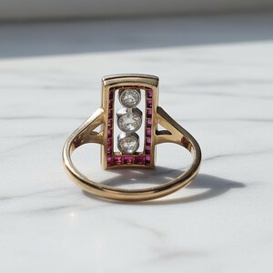Pu&ograve; includere: Un anello in oro con una testa rettangolare caratterizzata da una fila verticale di tre diamanti rotondi taglio brillante incastonati in metallo bianco. La cornice rettangolare &egrave; bordata da piccoli rubini rossi taglio quadrato su una fascia in oro giallo lucido.