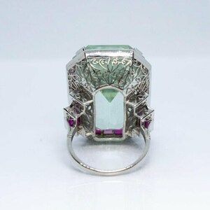 May include: A vintage platinum ring featuring a large, emerald-cut aquamarine stone surrounded by a delicate filigree design. The ring is accented with small ruby stones.