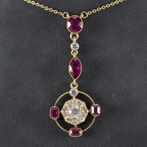 May include: A gold pendant necklace featuring a series of gemstones. The necklace has a gold chain and a pendant with a large oval ruby, a diamond, and a marquise-cut ruby. The pendant also has a circular design with diamonds and square rubies.