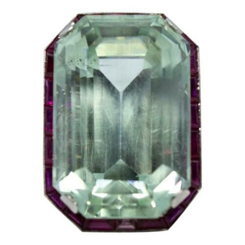 May include: A large, emerald-cut aquamarine gemstone set in a ring with a border of ruby stones.
