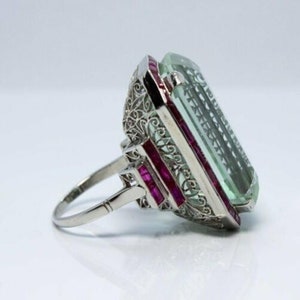 May include: A vintage ring featuring a large, emerald-cut aquamarine stone set in a filigree design with ruby accents.