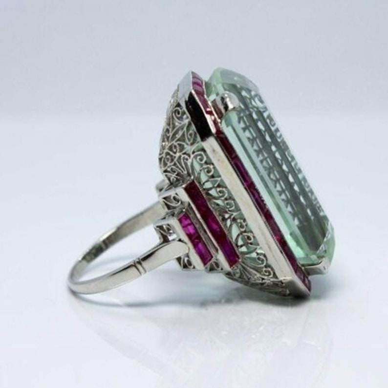 May include: A vintage ring featuring a large, emerald-cut aquamarine stone set in a filigree design with ruby accents.