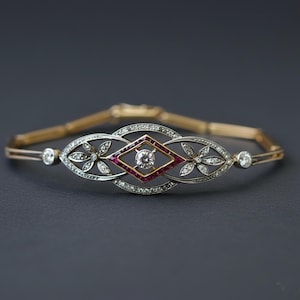 Puede incluir: Pulsera antigua de oro y plata con un diseño central de diamantes y rubíes. La pulsera presenta un diseño ovalado y floral con diamantes y un diamante en el centro. La pulsera mide aproximadamente 18 cm de largo.