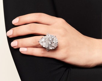 May include: A pear-shaped diamond ring set in a platinum band. The diamond is large and brilliant, with a classic cut. The ring is a statement piece of jewelry.