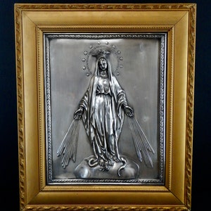 May include: A silver framed picture of the Virgin Mary in a gold frame. The image is embossed and shows the Virgin Mary with a crown of stars and rays of light emanating from her hands. The text around the image reads "Immaculate Conception".