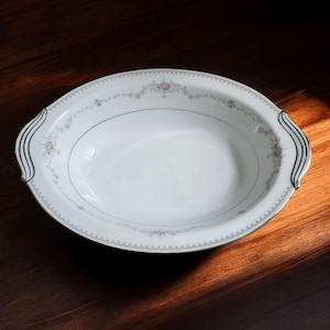 May include: White oval serving bowl with a floral pattern and black trim. The bowl has two handles on the sides.