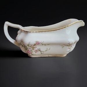May include: A white porcelain gravy boat with a gold rim and a floral pattern in pink and green.