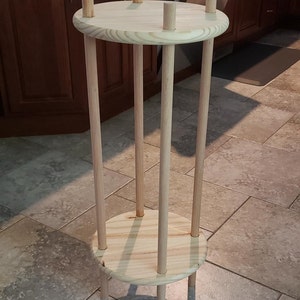 May include: A wooden plant stand with a round top and bottom shelf. The stand is made of natural wood and has a simple design.