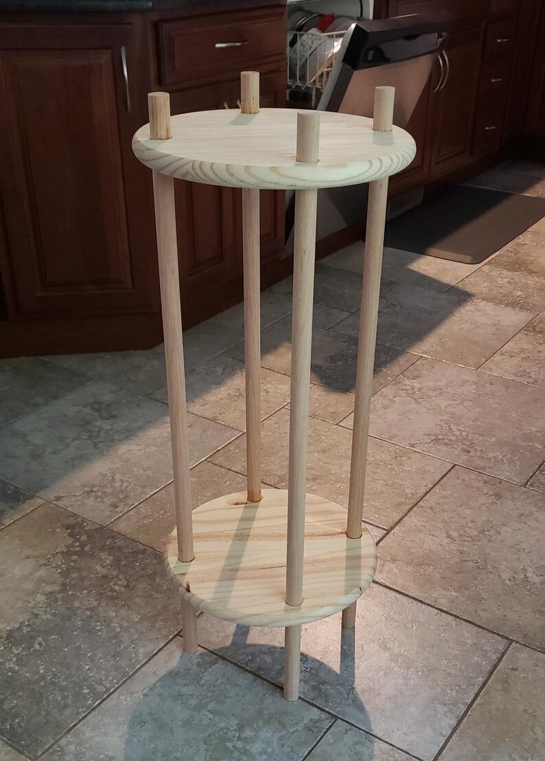 May include: A wooden plant stand with a round top and bottom shelf. The stand is made of natural wood and has a simple design.
