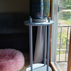 May include: A light blue plant stand with two round shelves and four legs. A potted plant with green leaves sits on the top shelf.