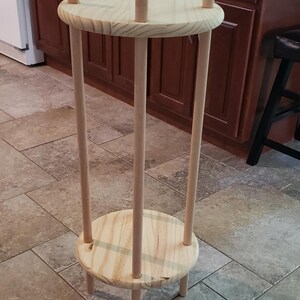 May include: A wooden plant stand with three legs and two circular shelves. The stand is made of natural wood and has a rustic look.