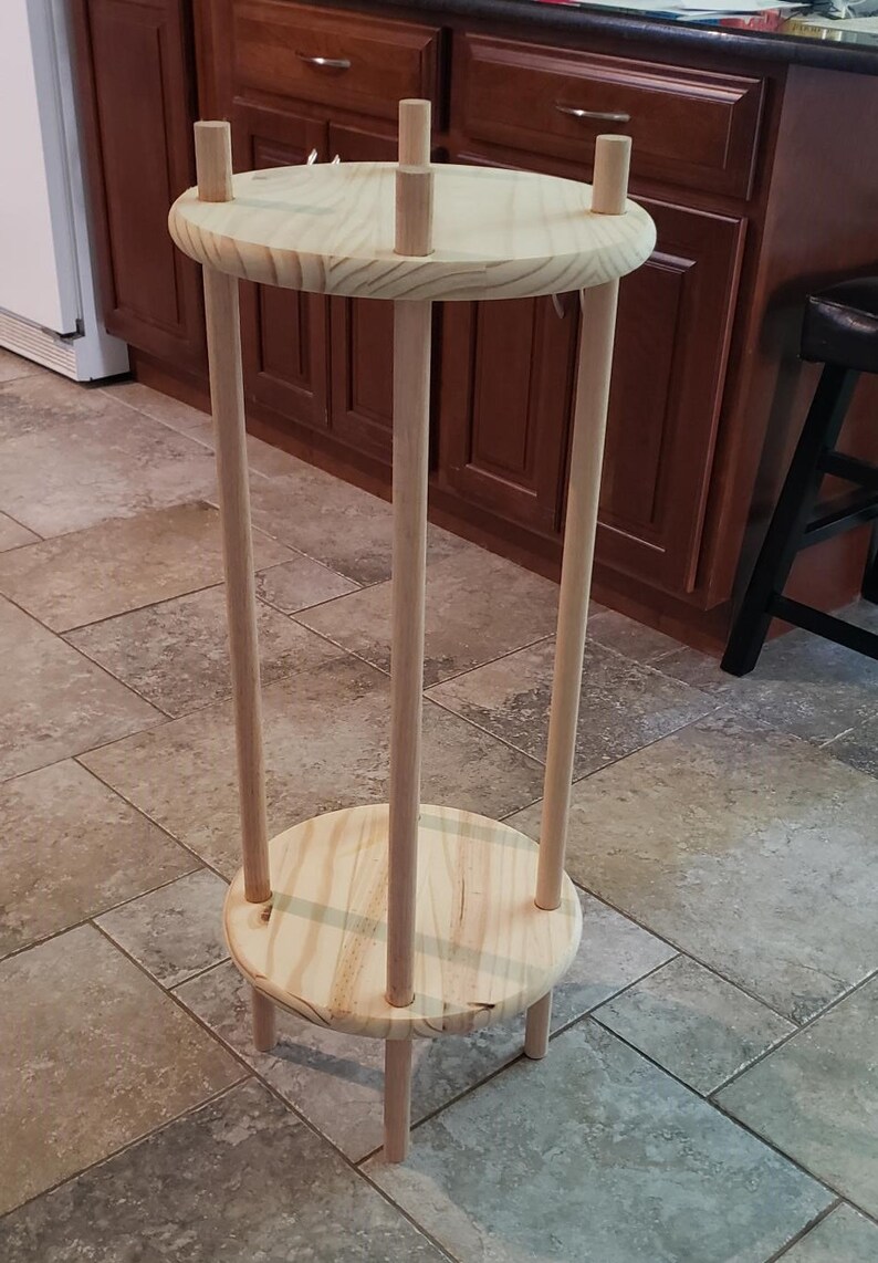 May include: A wooden plant stand with three legs and two circular shelves. The stand is made of natural wood and has a rustic look.