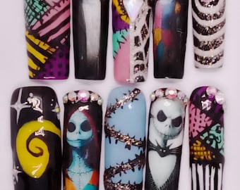 Puede incluir: Un conjunto de diez uñas postizas largas en forma de ataúd con varios diseños. Los diseños incluyen imágenes de Jack Skellington y Sally de The Nightmare Before Christmas, junto con patrones abstractos y detalles de purpurina. La paleta de colores incluye negro, blanco, rosa y morado.