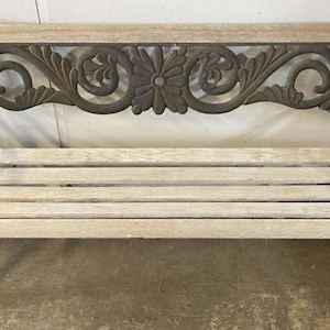 May include: A vintage outdoor bench with a decorative cast iron back featuring a floral design. The bench has light-colored wooden slats for the seat and a dark metal frame. A classic piece for a garden or patio.
