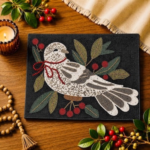 May include: A black beaded placemat featuring a detailed bird design with white, brown, and gold beads. The bird is adorned with a red bow and surrounded by beaded leaves and berries. A decorative item for the dining table.