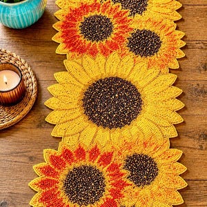 May include: A beaded sunflower table runner with yellow and orange petals and a brown center. The runner is made of small beads and is placed on a wooden surface. The runner is approximately 60 inches long.