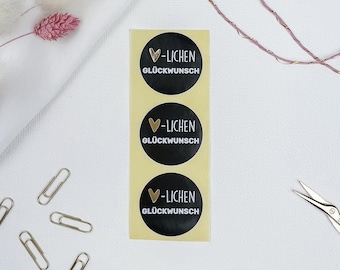 May include: Three black and gold round stickers with a heart and the text "Lichen Glückwunsch" on a white background.