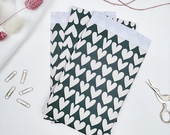 May include: Three green gift bags with white heart patterns. The bags are folded and stacked on top of each other.