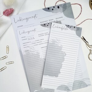 May include: Two gray recipe cards with a gray and white abstract design. The top card has the text "Lieblingsrezept" and the bottom card has the text "Einkaufsliste".