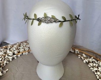 May include: A green leaf crown with a silver metal accent. The crown is on a white mannequin head.