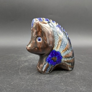 May include: A ceramic fish ornament with a brown body, blue and white detailing, and a blue flower. The fish has a detailed design and a glossy finish. The ornament is a decorative item.