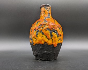 Puede incluir: Un jarrón de cerámica con un esmalte negro y naranja. El jarrón tiene un cuerpo redondo y un cuello estrecho.