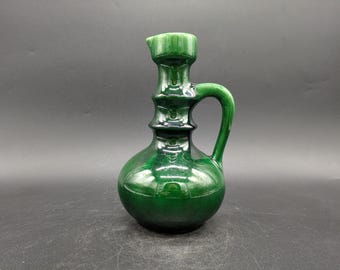 May include: A green ceramic pitcher with a wide mouth and a handle. The pitcher has a textured surface and a rounded body.