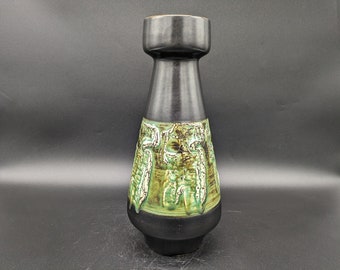 May include: A tall, black ceramic vase with a textured, green and brown design around the middle. The vase has a flared base and a cylindrical neck, with a slightly wider top. The overall shape is elongated and elegant.