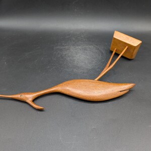 May include: A wooden sculpture of a bird with a long beak and a rectangular block attached. The bird is brown and has a sleek, streamlined design. The block is also brown and appears to be a separate piece.