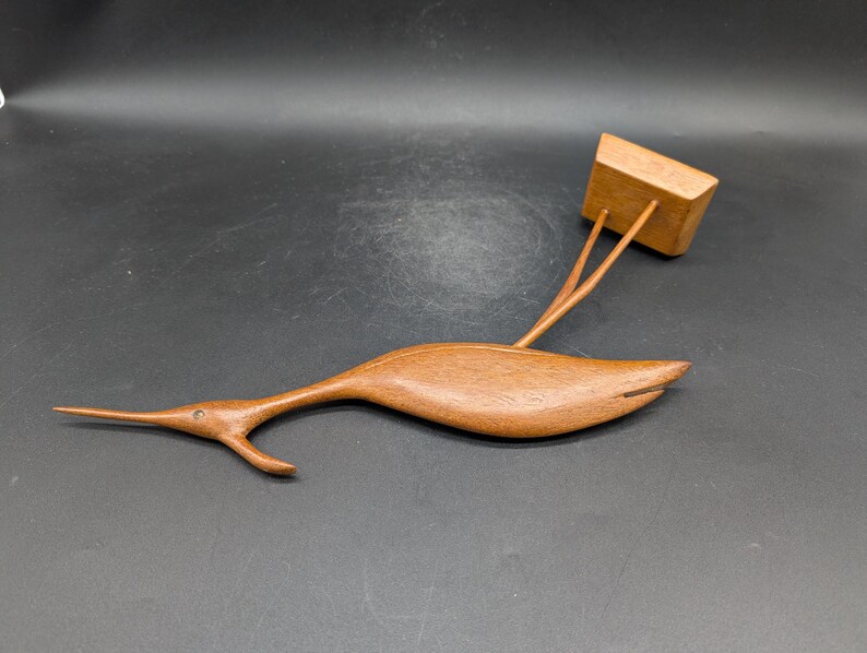 May include: A wooden sculpture of a bird with a long beak and a rectangular block attached. The bird is brown and has a sleek, streamlined design. The block is also brown and appears to be a separate piece.