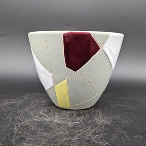 May include: A grey ceramic bowl with a geometric design in white, yellow, and burgundy.