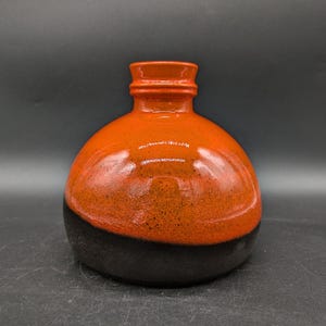 Könnte beinhalten: Eine Keramikvase mit schwarzer und orangefarbener Glasur. Die Vase hat einen runden Körper und eine breite Öffnung.