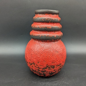 May include: A red and black ceramic vase with a textured surface and a layered design. The vase has a round body and a narrow neck.