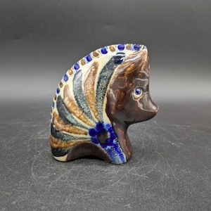 May include: A ceramic figurine of a horse with brown, blue and white painted details. The horse has a stylised mane and tail.