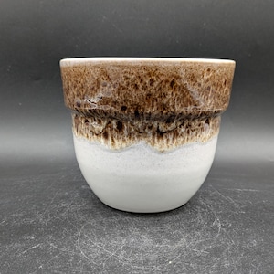 Può includere: Un vaso di ceramica bianca con una glassa marrone. La glassa ha un effetto marmorizzato, creando un motivo unico.