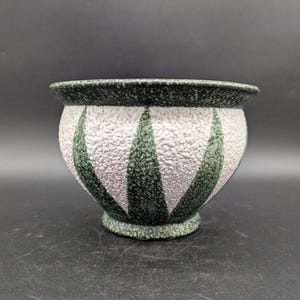Könnte beinhalten: Ein grüner und weißer Keramiktopf mit strukturierter Oberfläche und geometrischem Muster. Der Topf hat einen breiten, runden Boden und einen leicht ausgestellten Rand.