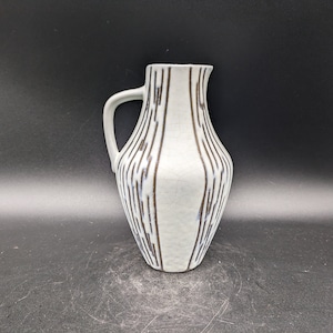 May include: A white ceramic pitcher with a brown and blue geometric pattern. The pitcher has a handle and a rounded body.