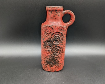 May include: A red ceramic vase with a black swirl pattern. The vase has a handle and a narrow neck.
