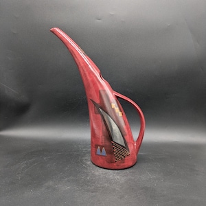 Może przedstawiać: Czerwony dzbanek ceramiczny z długim dzióbkiem i uchwytem. Dzbanek ma geometryczny wzór w kolorze czarnym, złotym i niebieskim.