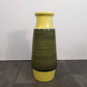 Könnte beinhalten: Eine gelbe und grüne Keramikvase mit geometrischem Muster. Die Vase hat einen breiten Boden und einen schmalen Hals.