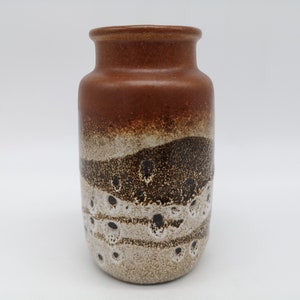 Puede incluir: Un jarrón de cerámica marrón, blanco y negro con un esmalte moteado. El jarrón tiene un cuerpo redondeado y una abertura estrecha.