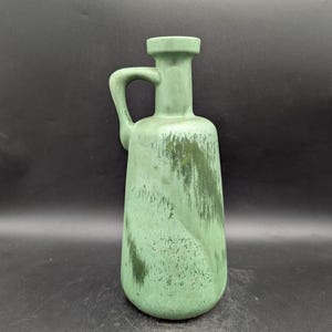 May include: A green ceramic vase with a handle. The vase has a textured surface with darker green streaks. The vase is approximately 10 inches tall.