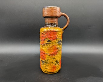 Może przedstawiać: Żółto-pomarańczowy ceramiczny wazon z brązową górą i uchwytem. Wazon ma fakturowaną powierzchnię i geometryczny wzór.