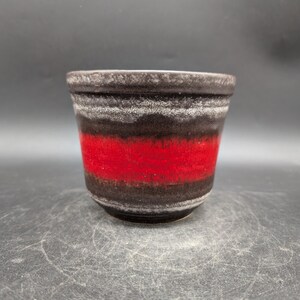 Peut inclure: Un pot de fleurs en céramique de forme cylindrique. Le pot présente une bande rouge vif au centre, encadrée de bandes marron foncé et blanches. Le bord et la base sont marron foncé. Convient pour une utilisation intérieure ou extérieure.
