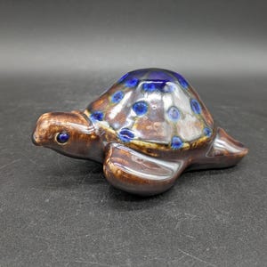 May include: A brown ceramic turtle figurine with blue and white accents. The turtle's shell has a speckled pattern and a glossy finish.