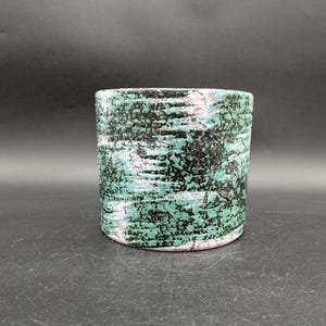 Peut inclure: Pot cylindrique en céramique à surface texturée. Le pot présente un motif moucheté de turquoise, de noir et de blanc, créant une esthétique organique unique. Convient pour les plantes ou comme objet décoratif.