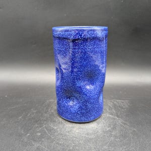 Könnte beinhalten: Ein Set aus drei Keramikbechern mit gesprenkelter, matter Oberfläche. Die Becher sind in Creme-, Hellgrau- und Dunkelgrautönen gehalten. Jeder Becher hat ein schlichtes, minimalistisches Design, perfekt für Kaffee oder Tee.