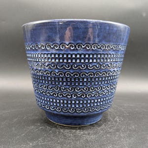 May include: A blue ceramic planter with a white geometric pattern. The planter has a wide mouth and a rounded bottom.