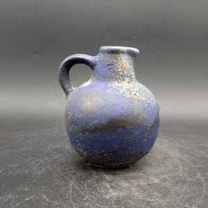 Könnte beinhalten: Ein kleiner blauer Keramik Krug mit einer strukturierten Oberfläche. Der Krug hat einen runden Körper und einen kleinen Henkel.