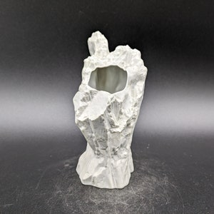 Peut inclure: Vase en céramique blanche en forme de souche d'arbre avec une surface rugueuse et texturée. Le vase a une ouverture ronde en haut.